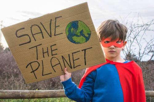 Little Boy Pretending To Be A Superhero With A Red Cape, Holding A Cardboard Sign That Says SAVE THE PLANET